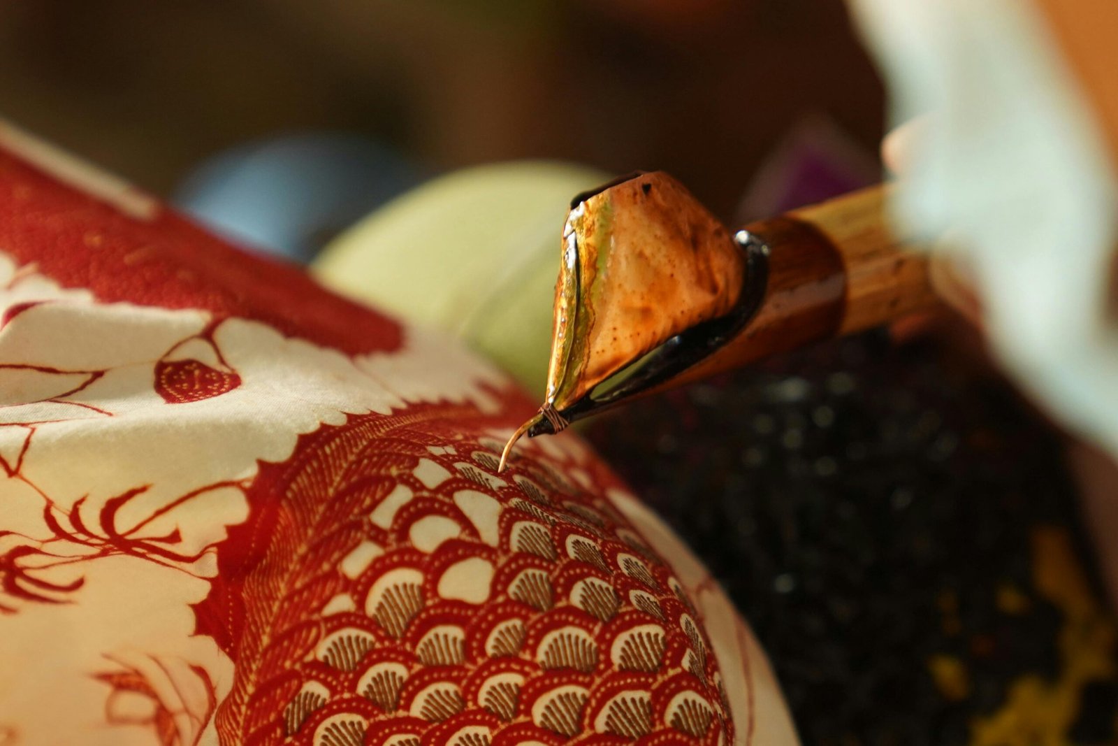 Close-up of canting tool applying wax on cloth for traditional batik design.